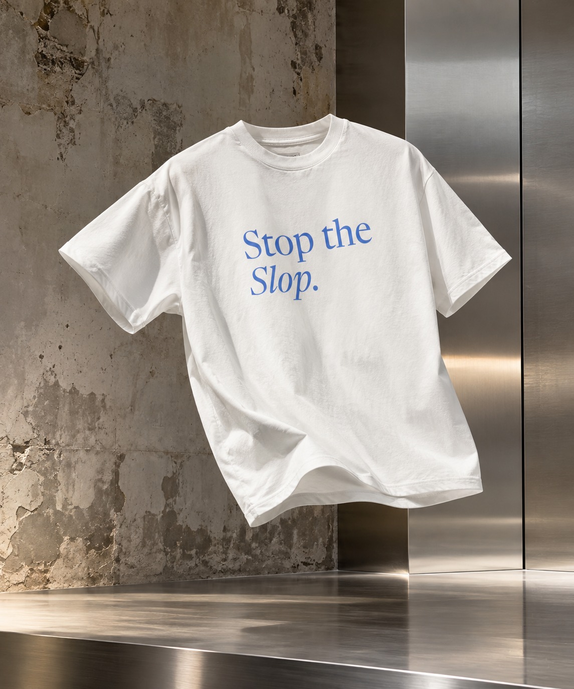 White Stop the Slop tee with blue lettering, floating against concrete and brushed steel